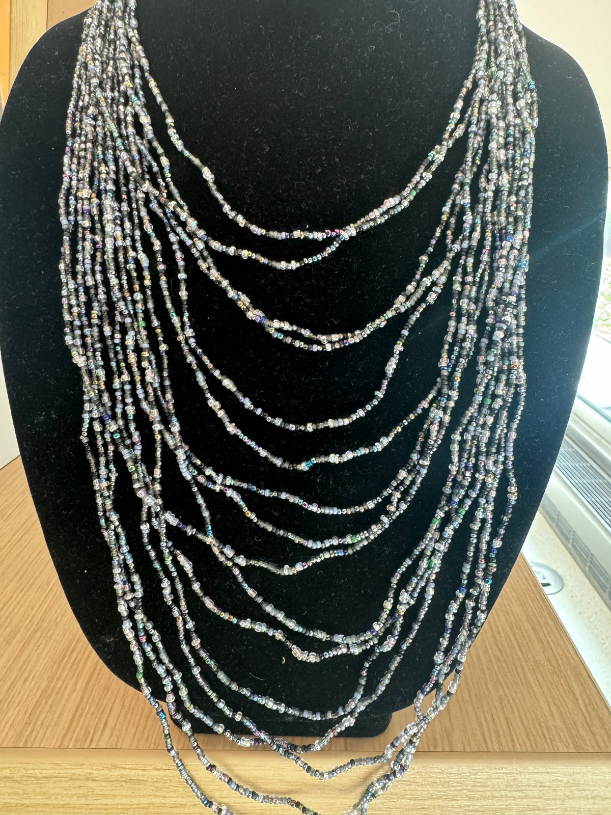 Multi-strand necklace of gray and iridescent beads on a black display