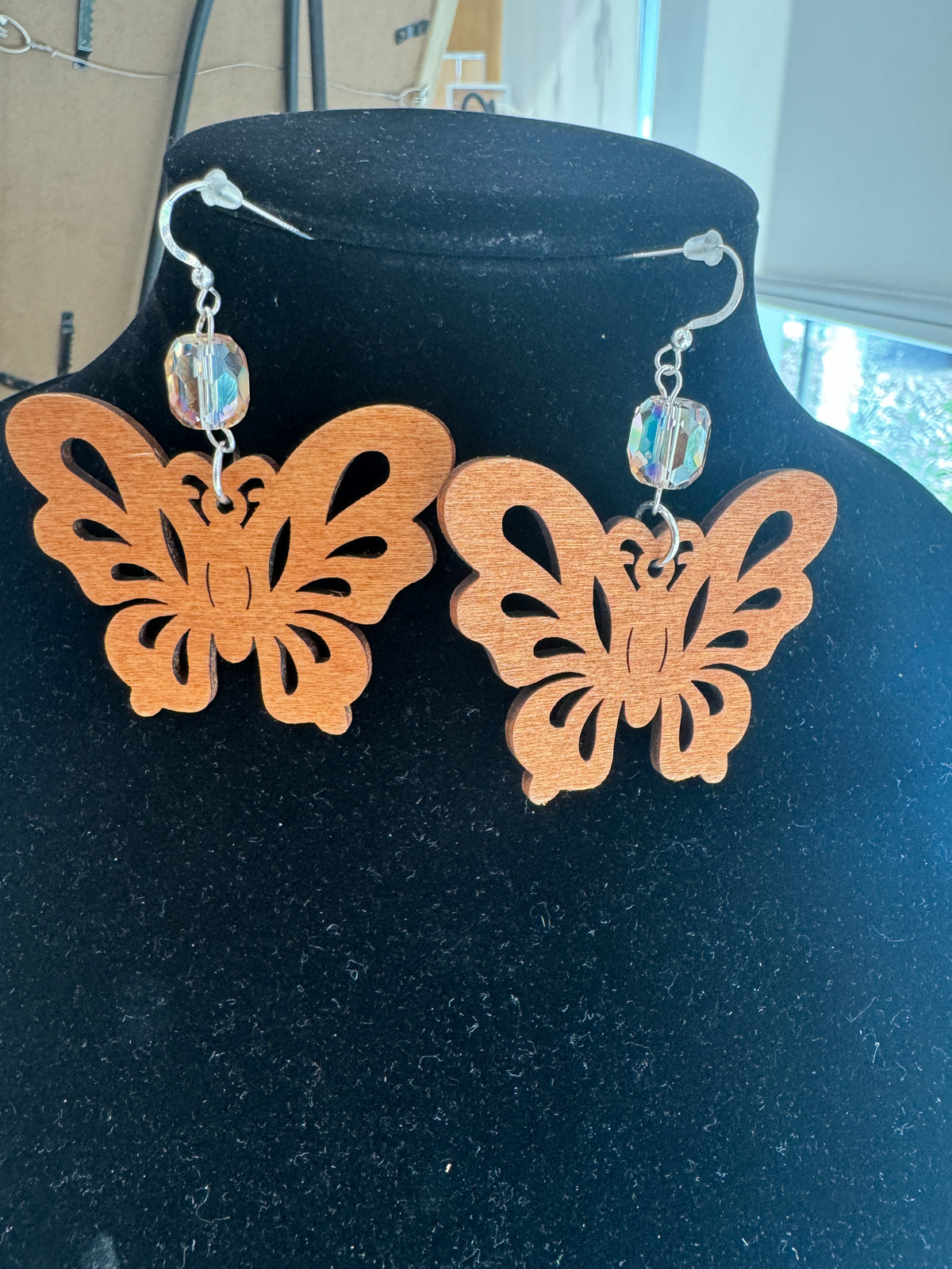 Openwork wooden butterfly earrings with faceted crystal accents on a black display